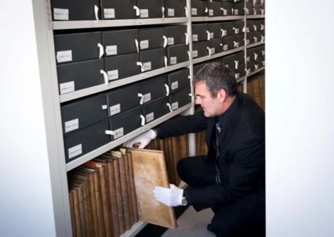 Conservation d'archives de marque : consultation d'un registre ancien devant des boîtes d'archives